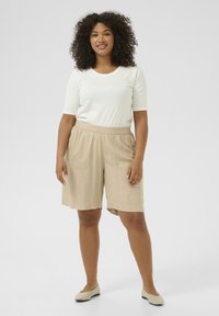 Shorts légers beiges avec une taille élastique, des poches latérales et une coupe décontractée, associés à un haut blanc ajusté à manches courtes.