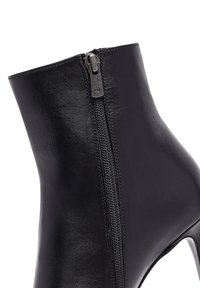 Bottine en cuir noir avec un talon haut et une fermeture éclair sur le côté, mettant en valeur une texture lisse avec une finition brillante et des détails en matériel YKK.