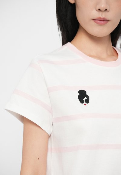 T-shirt branca com riscas rosa claras, decote arredondado, mangas curtas, apresentando um rosto bordado com cabelo preto e óculos de sol.