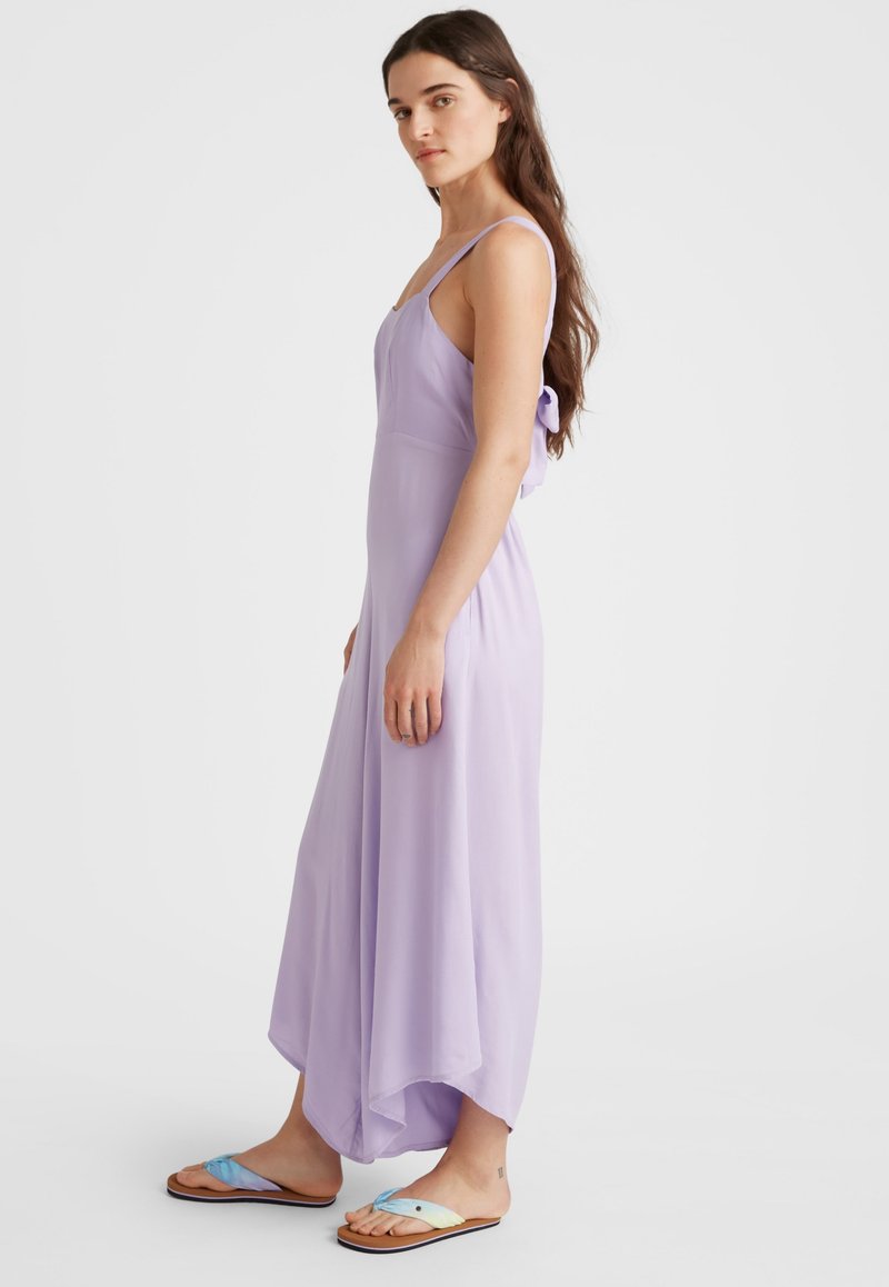 Helles lila ärmelloses Kleid mit fließendem Design, das hinten mit einer Schleife verziert ist und einen Saum bis zur Mitte der Wade hat. Getragen mit mehrfarbigen Flip-Flops.