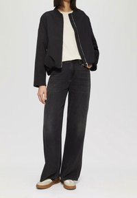 Czarna kurtka bomberka na kremowej koszuli, w zestawieniu z ciemnymi dżinsami wysokiego stanu o szerokich nogawkach oraz beżowo-białymi trampkami.