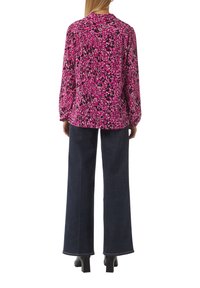 Blusa a maniche lunghe di colore rosa con motivo astratto in bianco e nero; vestibilità comoda; abbinata a jeans larghi scuri e scarpe con tacco quadrato.