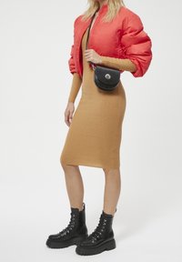 Giacca bomber imbottita rossa, vestito beige a coste, stivali neri con lacci alla caviglia e una piccola borsa a tracolla nera con chiusura in argento.