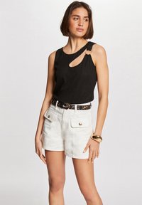Black sleeveless top with a curved cutout and silver ring detail; paired with white shorts featuring front pockets and gold-tone buttons.