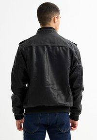 Chaqueta bomber de cuero negro con puños y dobladillo acanalados, hombreras y textura suave. Vista trasera que muestra un diseño minimalista.