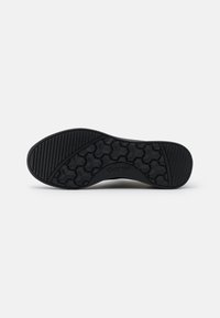 Black shoe sole with a textured hexagonal pattern and ridges for grip, featuring rounded edges and a smooth central segment.