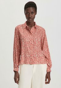 Blusa a maniche lunghe in tessuto leggero, con motivo floreale rosa su sfondo chiaro, chiusura frontale con bottoni e vestibilità rilassata.