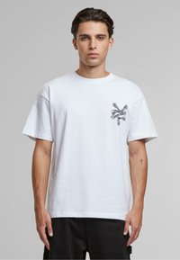 Hvid bomulds t-shirt med en afslappet pasform, korte ærmer og et sort dødningehoved med korslagte knogler grafik på venstre bryst. Minimalistisk design.