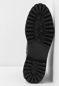 Mustan saappaan pohja syvillä urilla ja tähtikoristeilla, jossa on teksturoitu muotoilu. Merkitty "37" ja "TOMMY HILFIGER" -brändillä.