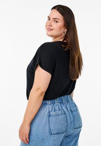 Svart avslappnad t-shirt med korta ärmar, ihop med hög midja ljusblå denimbyxor med elastisk midja och bakfickor.