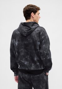 Casaco com capuz em tie-dye preto, com capuz ajustável por cordão, mangas compridas e punhos canelados. Tecido macio com acabamento texturizado.