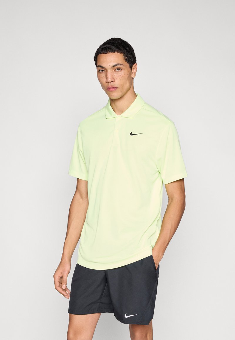 Polo Nike de couleur jaune fluo vif, avec un logo noir sur le côté gauche de la poitrine. Porté avec un short de sport noir, tissu lisse, coupe décontractée.