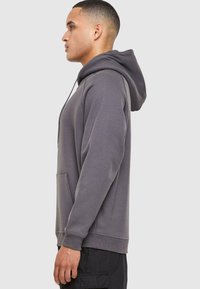 Sudadera con capucha gris, con bolsillo frontal, corte relajado y puños de canalé. Tela suave, cuenta con cordón y costuras laterales.