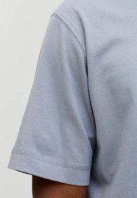 Lühikeste varrukatega heledashall T-särk, mis on valmistatud siledast kangast. Omab klassikalist ümmargust kaelust ja lihtsaid kahekordse õmblusega ääri.