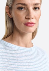 Chemise rayée bleu clair et blanche en tissu doux avec un col rond. Gros plan montrant les traits du visage et la texture de la peau lisse.