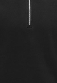 Sweat-shirt noir à fermeture éclair argentée, fabriqué en tissu doux. Il présente un col montant et des coutures nettes sans motifs.