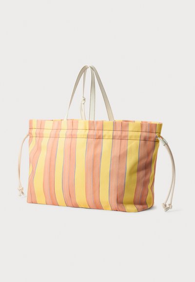 Sac fourre-tout rayé en jaune et pêche, avec des lignes bleu clair. Fabriqué en tissu, il dispose d'une fermeture coulissante et de deux poignées supérieures.