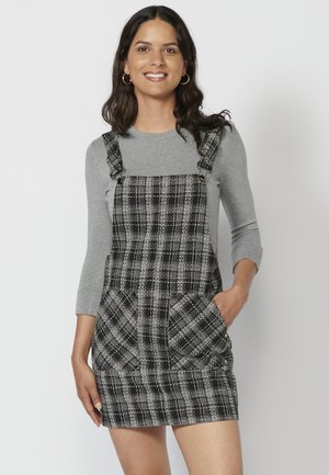 Robe salopette à carreaux noir et blanc avec deux poches avant, bretelles réglables, assortie à un haut à manches longues gris clair. Texture de tissu lisse.