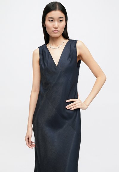 Αμάνικο, σκούρο ναυτικό φόρεμα με V λαιμόκοψη, λεία σατέν υφή και διαγώνιες ραφές. Διακοσμημένο με ένα κοσμηματοθήκη.