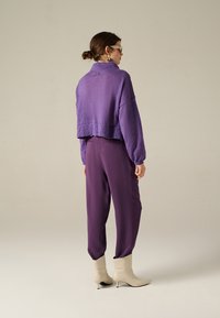 Maglione viola, accorciato e strutturato abbinato a pantaloni viola a vita alta e stivaletti crema con punta. Design semplice e aderente.