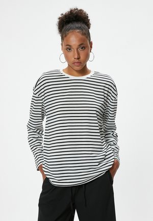 Chemise à manches longues rayée noir et blanc avec un col rond ; coupe décontractée ; le tissu semble doux avec un léger éclat ; portée avec un pantalon noir.