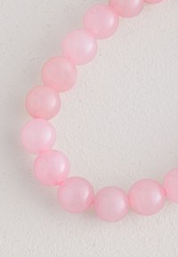 Rosa Perlenarmband mit glatten, glänzenden runden Perlen aus halbtransparentem Material, die zu einem kreisförmigen Design aufgereiht sind.