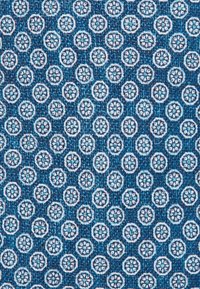 Blauwe gestructureerde stof met een herhalend patroon van kleine witte cirkelvormige motieven met bloemdecoraties in het midden, gelegen tegen een donkerdere blauwe achtergrond.