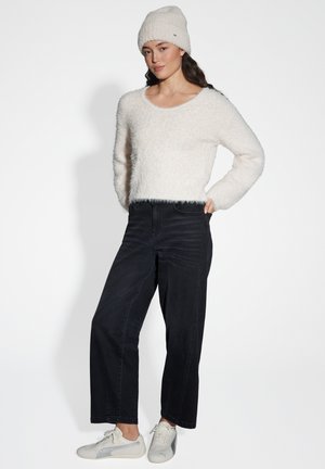White, fluffy textured sweater paired with high-waisted, straight black jeans and light grey sneakers. Model stands with hands in pockets.