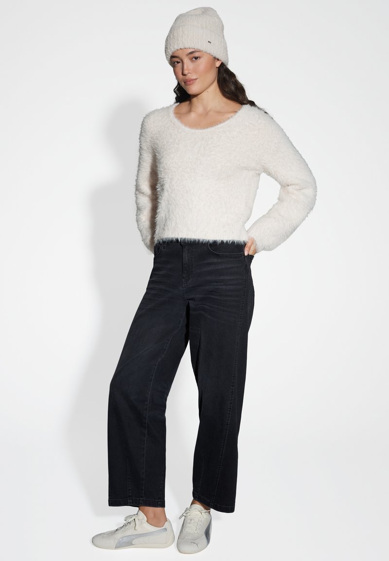 White, fluffy textured sweater paired with high-waisted, straight black jeans and light grey sneakers. Model stands with hands in pockets.