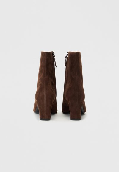 Brown suede ankle boots with a tapered shape, block heels, and side zippers, featuring a smooth texture and minimalistic design.