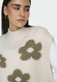 Strickweste mit hohem Kragen, in zartem Rosa, mit großen olivgrünen Blumenmustern, weicher Textur und ärmellosem Design.