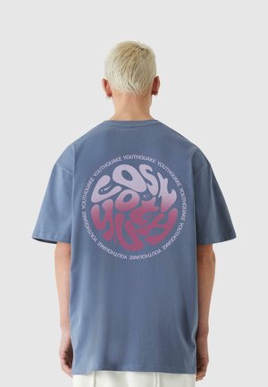 T-shirt en coton bleu avec un graphique arrondi en texte rose et violet au dos, mettant en avant le mot "Youthquake" dans un motif circulaire.