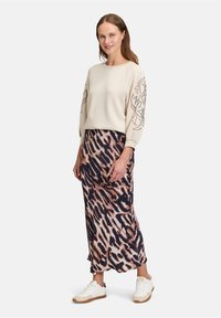 Pull beige avec des découpes décoratives sur les manches, associé à une jupe maxi imprimée animal en marron et noir. Des baskets blanches complètent le look.