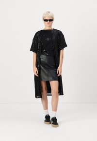 Kimono negru cu paiete peste un tricou negru cu un model subtil, combinat cu o fustă din piele neagră, șosete albe și adidași negri.