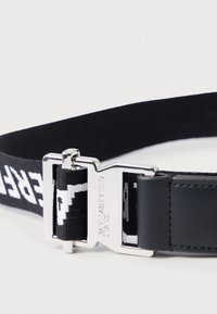 Cinto em tecido trançado preto e branco com fecho de metal prateado gravado com "KARL LAGERFELD JEANS" e detalhe em couro preto anexado.