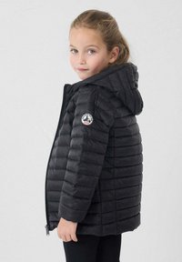 Giacca imbottita nera con cappuccio, caratterizzata da un motivo trapuntato orizzontale, cerniera frontale e una toppa rotonda sulla manica sinistra.