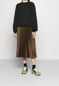 Svart sweatshirt med puffärmar, kombinerad med en plisserad brun midikjol. Bärs med svarta strumpor och atletiska skor med neons accent.