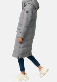 Szary ocieplany płaszcz z kapturem, z zapięciem na zamek, z zamykanymi bocznymi kieszeniami oraz z naszywką z logo na rękawie. Nosi się go z niebieskimi dżinsami i białymi trampkami.