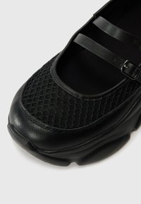 Scarpa nera con tomaia in rete testurizzata, dettagli con doppia cinghia e accenti in finta pelle liscia. Punta arrotondata e suola imbottita per il comfort.
