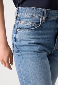 Hoge taille blauwe denim jeans met een gladde textuur, vijf zakken, koperen klinknagels en subtiele vervaging op de stof. Sluit nauw aan.