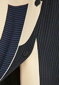 Tissu rayé avec des couleurs marine et crème, doté d'un bouton noir plat, d'une texture lisse et d'éléments de design superposés.