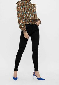 Blus med blommönster och volanger vid axlarna, ihopparad med svarta slim-fit jeans och blå spetsiga klackar.