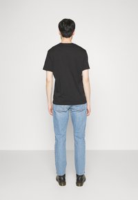 Camiseta de algodón negra con cuello redondo, combinada con jeans de mezclilla azul claro y calzado negro, vista desde atrás. Diseño simple.