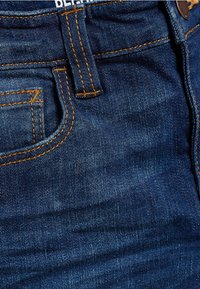 Jeans in denim blu scuro con cuciture gialle, dotati di tasca frontale e vita con bottone e passanti per cintura.