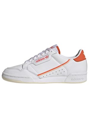 Biały niski but Adidas z pomarańczowymi akcentami, perforowanym bocznym panelem oraz firmowymi logo na boku, języku i pięcie.