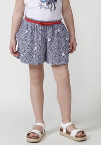 Pantaloni corti a righe blu navy e bianchi con una cintura rossa, dotati di tasche laterali. La texture è liscia e il design presenta motivi a spirali e pesci.