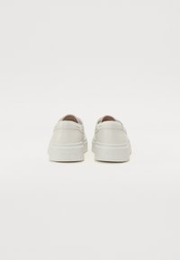 Hvite sneakers med en glatt lærtekstur, rund form, polstret krage og en tykk gummisåle. Har preget merkevare på hælen.