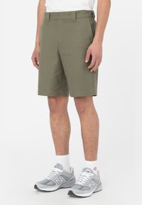 Pantaloni corto verde oliva realizzati in tessuto misto cotone, con taglio dritto, passanti per cintura e tasche frontali, abbinati a scarpe da ginnastica grigie.