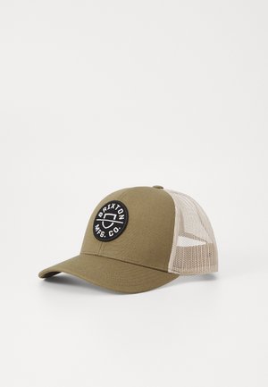 Khaki baseballcap med mesh bak, rund svart lapp med "Brixton Mfg. Co." logo, buet skjerm og strukturert frontpanel.