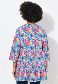 Tunika floreale colorata con scollatura rotonda, maniche a tre quarti e vita arricciata; presenta un mix di motivi rosa, blu e verdi.